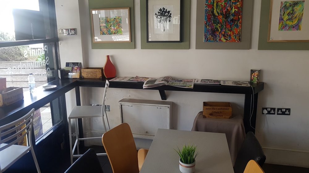 A table and chairs by the wall with a small potted plant and framed prints